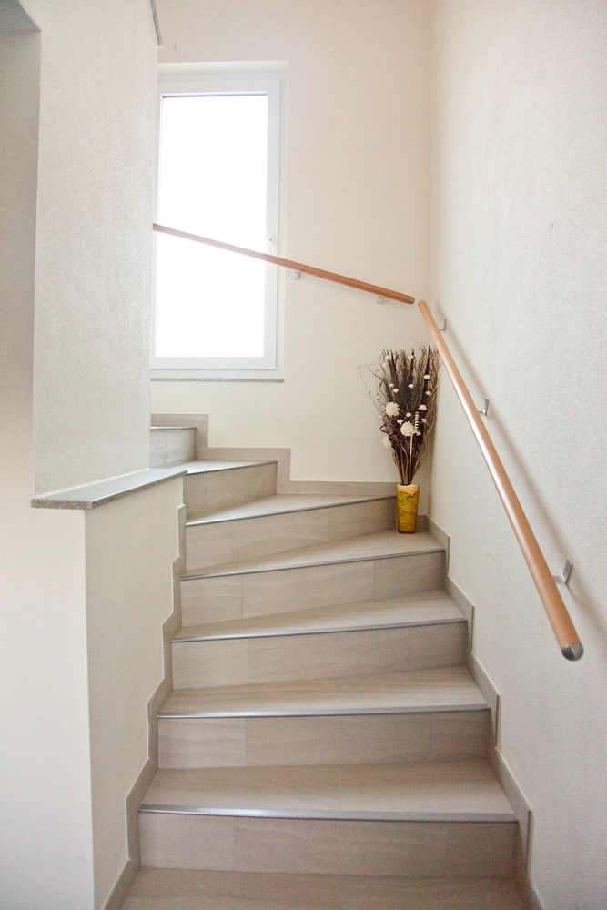 Ferienwohnung Greiler – Innenraum; Vorraum bzw. helles Stiegenhaus mit Treppe aus schönen grauen Fliesen, sowie ein Holzgriff zum festhalten, gepflegte Ausstattung.